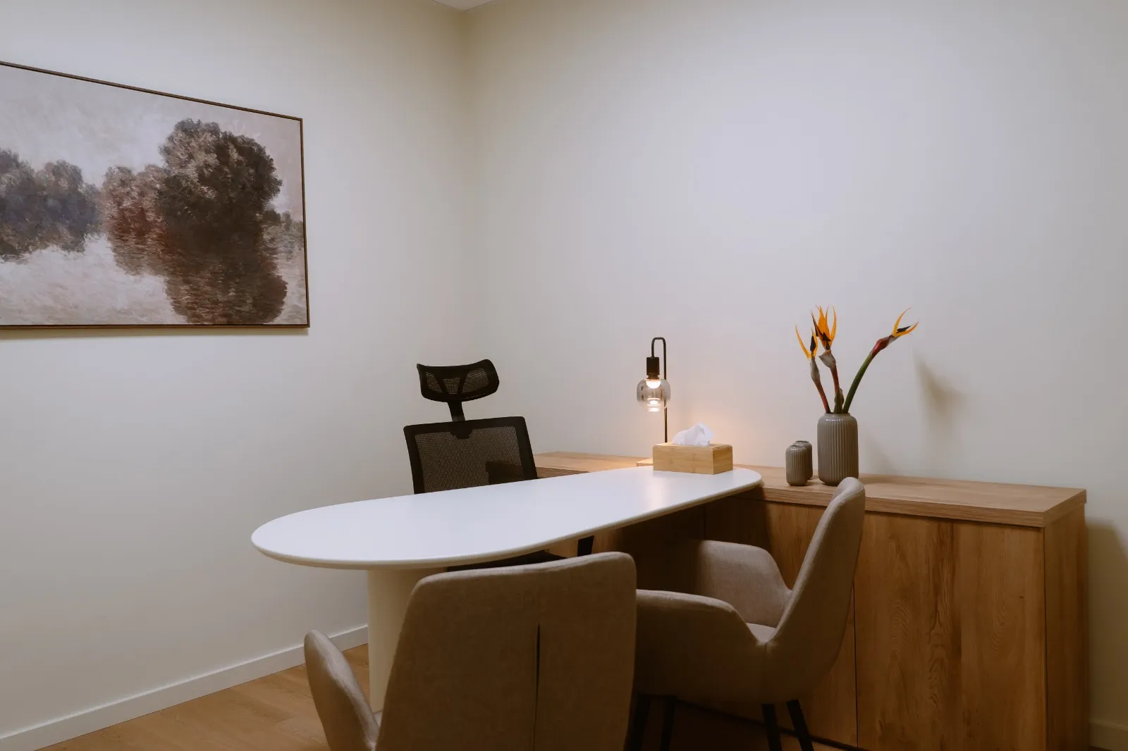 Sala de consulta com quadro na parede, mesa branca e flores